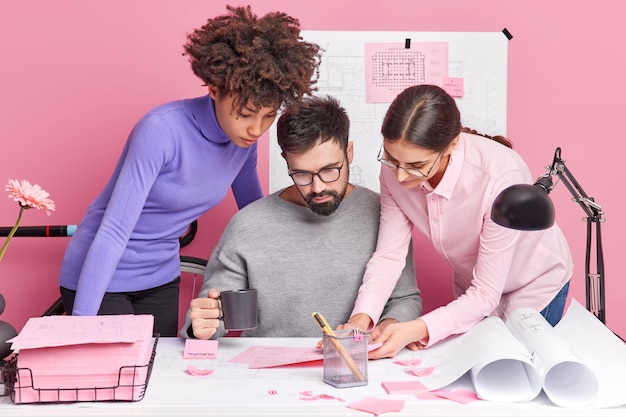 Crew of diverse skilled women and man coworkers share ideas while making future project focused at papers pose together at desktop cooperate for common task have attentive gazes. Teamwork concept