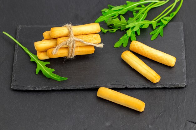 Crispy bread sticks with arugula, bread sticks on black stone background with copy space.