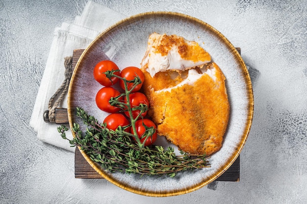 Crispy breaded tilapia filles on a plate with vegetables White background Top view