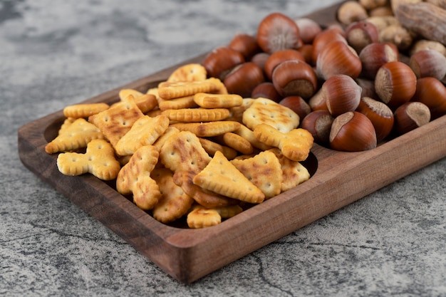 Crispy crackers with hazelnuts and peanuts in shell on a wooden board . 