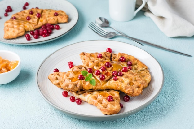 Crispy croffles with red currants, honey and mint on plates and a cup of coffee  on a light table. Sweet delicious breakfast. Close-up