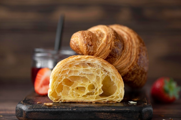 Crispy croissants with fresh strawberries and jam on a wooden board