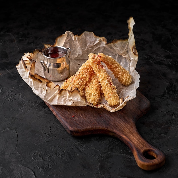 Crispy fried chicken nuggets with tomato sauce. Tasty snack for beer on a dark background