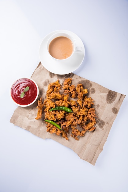 Crispy Kanda bhaji or Bhajji or Pyaj Pakode or fried onion pakora, delicious street food, favourite indian snack in monsoon served with tomato ketchup and Hot Tea