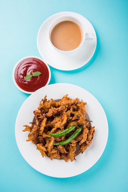 Crispy Kanda bhaji or Bhajji or Pyaj Pakode or fried onion pakora, delicious street food, favourite indian snack in monsoon served with tomato ketchup and Hot Tea