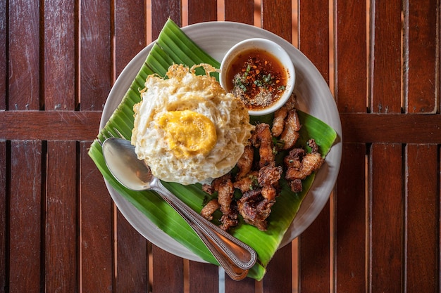 Crispy pork belly served with fried egg steamed rice and sweet spicy sauce in ceramic dish