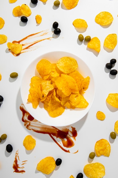 Crispy potato chips in a white plate scattered on a white background Top view flat lay