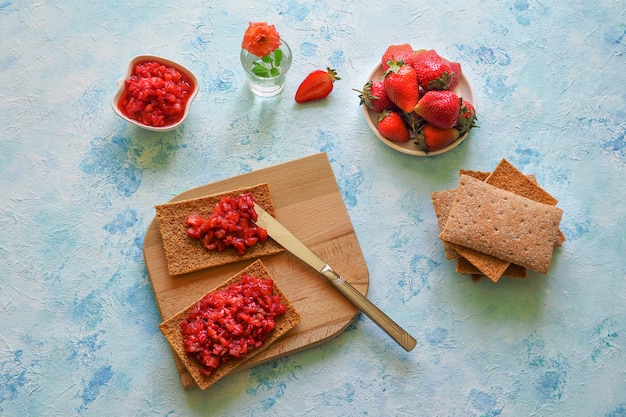 Crispy rye with strawberry jam. Strawberry toast on rye bread. Vegetarian sweet breakfast on a white on a blue surface