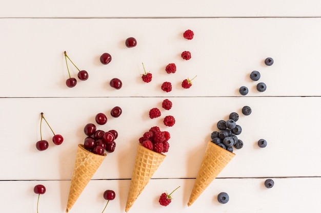 Crispy waffle cones with summer berries on a white wooden table. refreshing dessert.