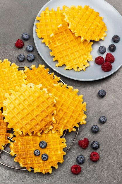 Crispy waffles on gray plate and metal stand Raspberries and blueberries on table