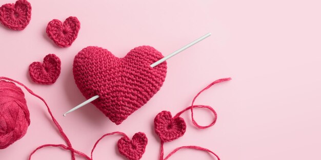 Crocheted amigurumi purple red burgundy hearts with crochet hook on a pink background Valentine's day banner