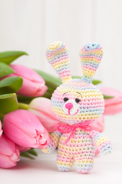 Crocheted rabbit with delicate pink tulips.  Knitted toy, handmade, needlework, amigurumi.