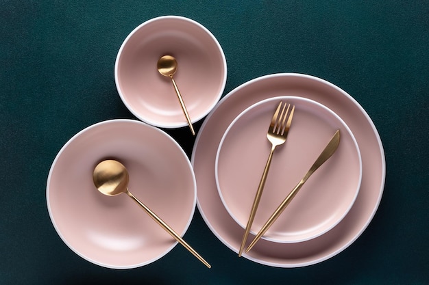 Crockery and golden cutlery on a dark green background table top view above Flat lay design Ceramic empty plates utensils for serving Trendy tableware set for serving beige luxury dishes