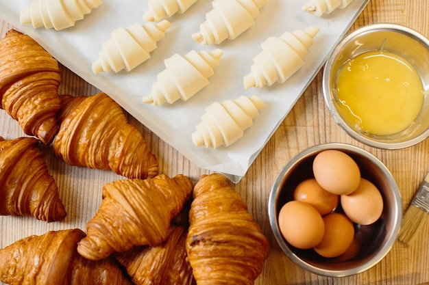 Croissant baking concept Raw rolled up and freshly baked croissants as well as ingredients lie on the table