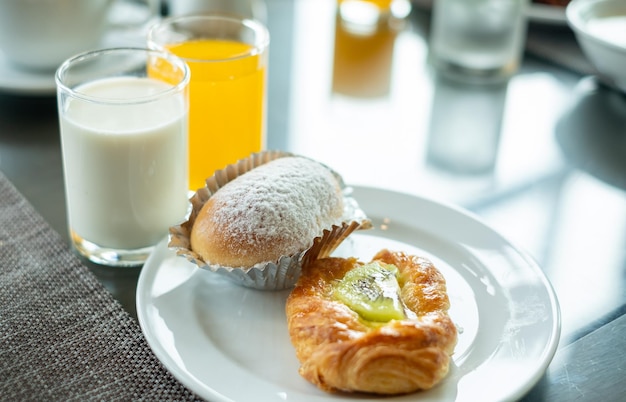 Croissant bread in a white plate with a glass of fresh milk and orange juice on the breakfast table