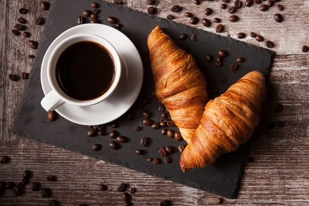 Croissant and cup of hot coffee on dark wooden table. Great breakfast.