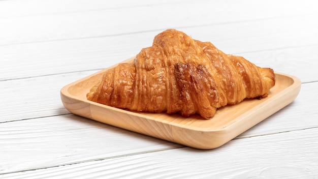 Croissant the delicious bakery in wooden plate on vintage white wooden background