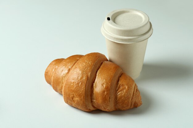 Croissant and paper cup on light gray