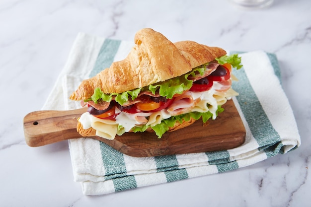 Croissant sandwich with cheese ham lettuce tomatoes olives and delicious sauce on wooden board