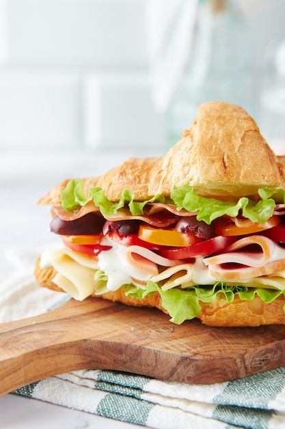 Croissant sandwich with cheese ham lettuce tomatoes olives and delicious sauce on wooden board