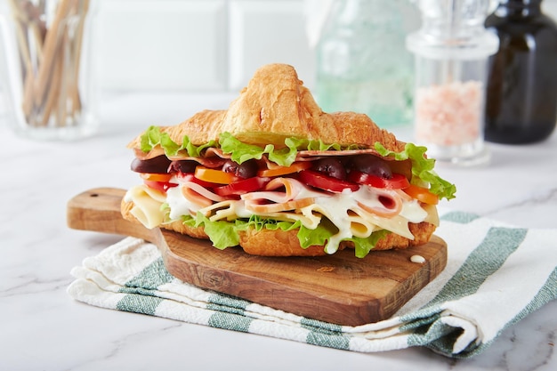 Croissant sandwich with cheese ham lettuce tomatoes olives and delicious sauce on wooden board