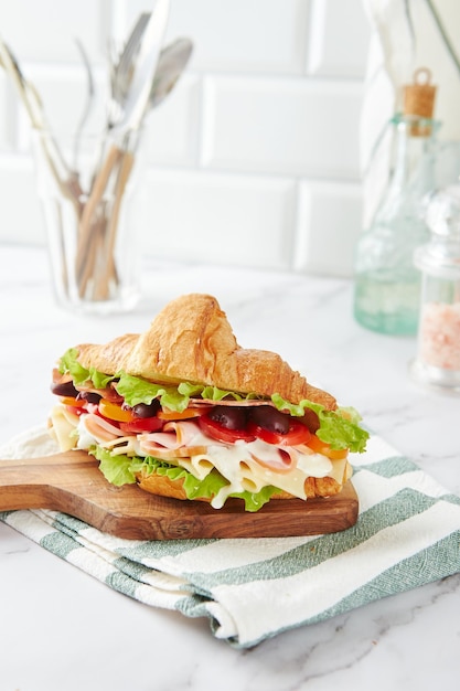 Croissant sandwich with cheese ham lettuce tomatoes olives and delicious sauce on wooden board