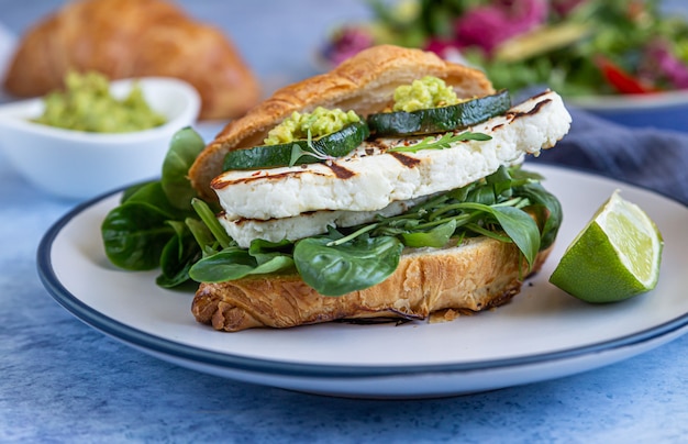 Croissant sandwich with grilled halloumi, arugula and grilled zucchini. Healthy breakfast or lunch.