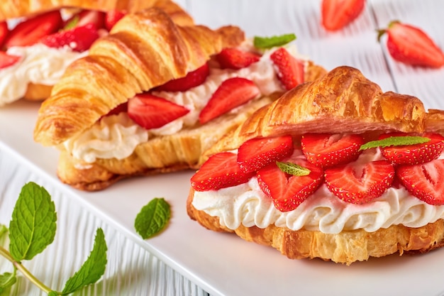 croissant sandwiches with fresh ripe strawberries and whipped cream cheese on a platter on white wooden table