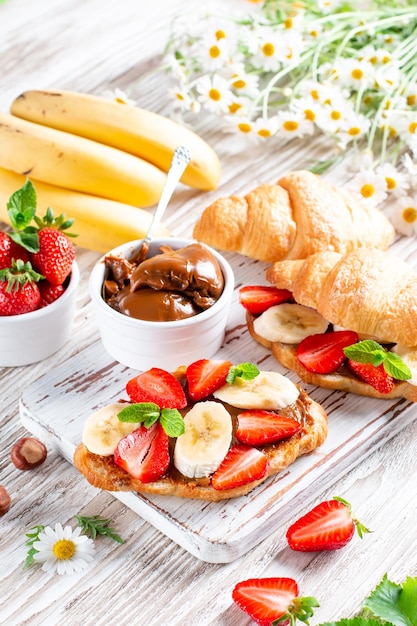 Croissant with banana peanut butter and strawberry on wooden board French pastry