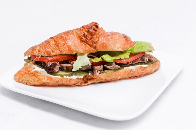 Croissant with beef pickled cucumber tomato and lettuce on a white background