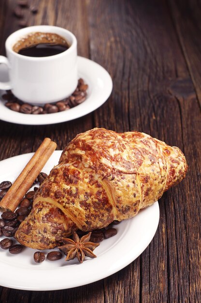 Croissant with cheese and cup of hot coffee for breakfast on old wooden table