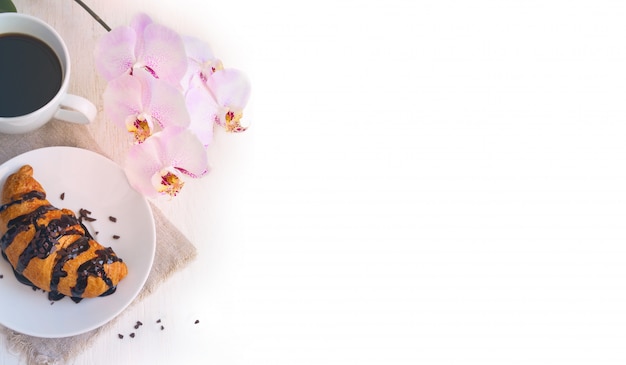 Photo croissant with chocolate, cup of coffee and a pink orchid on white background