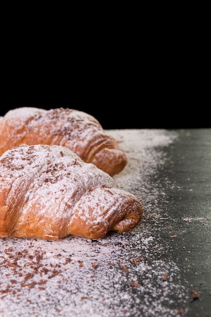 Croissant with chocolate and powdered sugar on black background. French dessert.