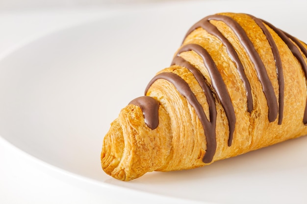 Croissant with chocolate stripes on white plate selective focus