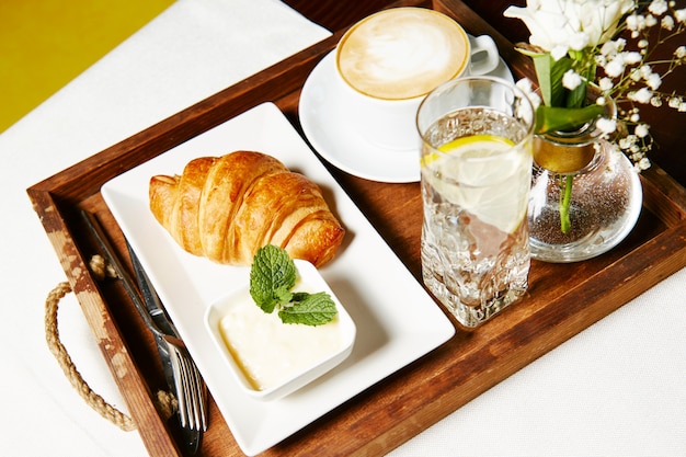 Croissant with pate and a glass of water with lemon on a tray