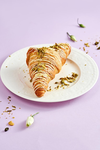 Croissant with pistachio cream and sprinkle of nuts on a white plate on a pink background