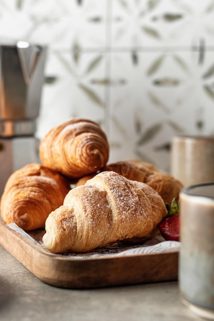 Croissants close up on wooden tray with berries and coffee for breakfast with tile background