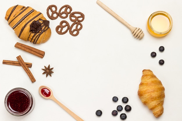 Croissants and figured cookies, berries, apricots honey, jam, cinnamon. Set of products for nutritious breakfast. White background. Flat lay. Copy space