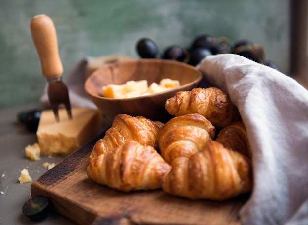 Croissants whit delicious cheese and grapes for tasty breakfast. Original tasty French croissants with cheese and grapes on the wooden table. buttery flaky viennoiserie bread roll distinctive crescent