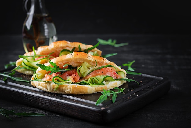 Croissants with salted salmon cucumber and arugula served on dark background Close up