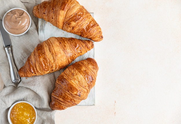 Croissants on wooden cutting board with jam and chocolate cream