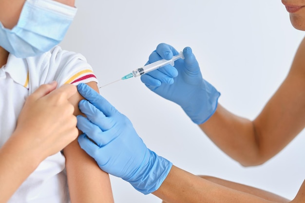 Crop anonymous female medic with syringe vaccinating patient during COVID 19 pandemic in clinic on white background