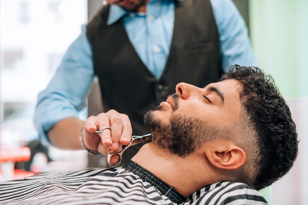 Crop barber cutting beard at barbershop