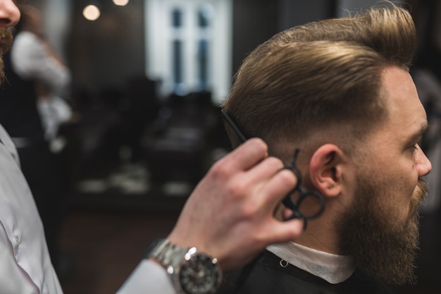 Crop barber cutting hair of bearded man