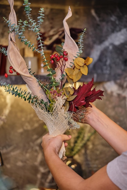 Crop faceless female demonstrating bouquet of dried flowers berries and eucalyptus branches in florist shop