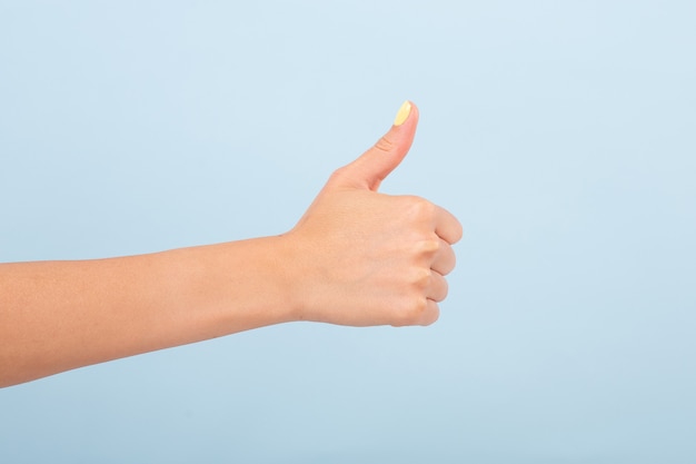 crop female hand with bright manicure holding thumb up in approve against plain light