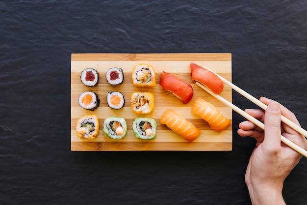 Crop hand picking sushi from board