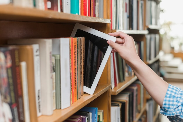 Crop hand taking tablet from bookshelf