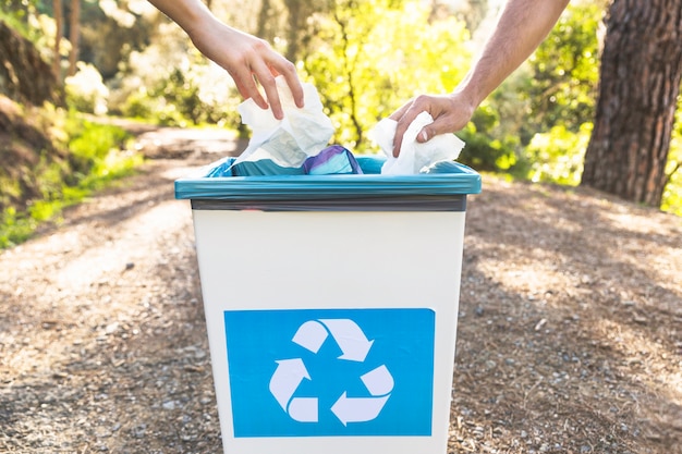 Crop hands throwing garbage in bin in forest