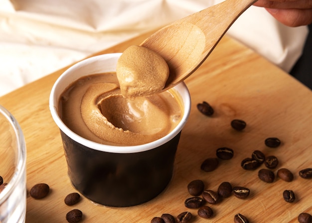 Crop image of hand scooping coffee ice cream in a paper cup with a wooden spoon